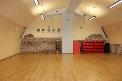 Pusta sala do ćwiczeń z parkietem, ścianą z cegieł i stepami, oświetlona lampami sufitowymi.