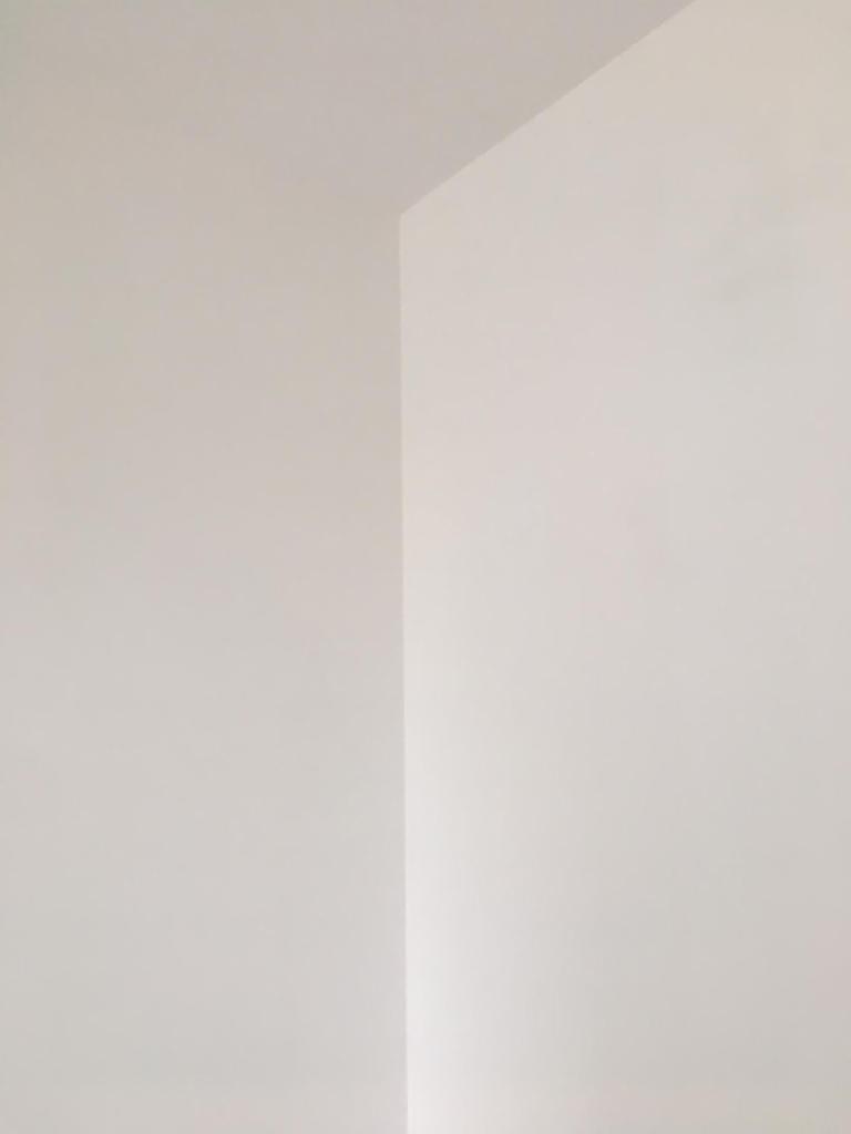 Wnętrze w stanie deweloperskim: gładkie, białe ściany i sufit, narożnik pokoju pod delikatnym kątem, gotowe do dalszych prac wykończeniowych.