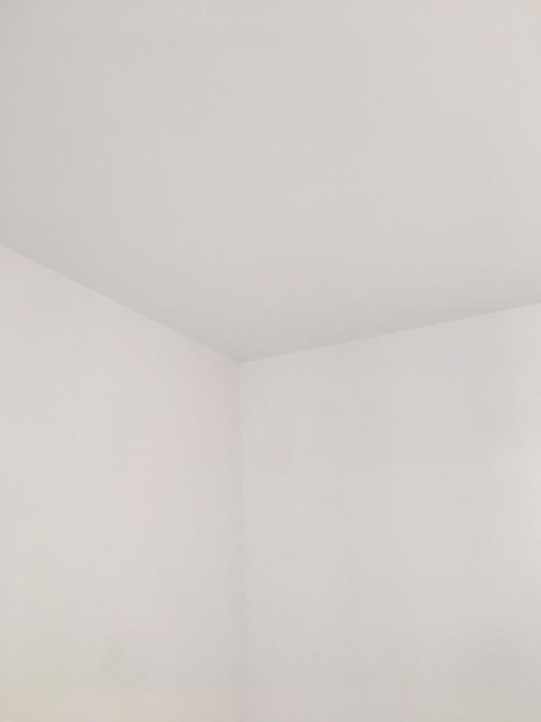 Róg pokoju w stanie deweloperskim, białe, zagruntowane ściany i sufit gotowe do dalszych prac wykończeniowych, widoczne delikatne załamania światła.