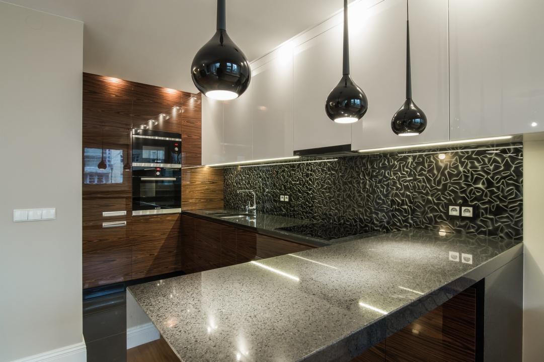 Nowoczesna kuchnia z drewnianymi i białymi szafkami, czarnym wzorzystym panelem nad blatem i trzema czarnymi lampami wiszącymi w kształcie kropli.