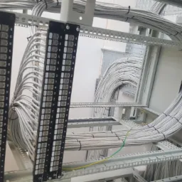 Panel krosowniczy z numerowanymi portami i uporządkowane wiązki kabli w metalowej szafie serwerowej, widoczne fragmenty okablowania strukturalnego.