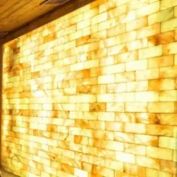 Ściana sauny wyłożona podświetlanymi cegłami solnymi, widoczny fragment drewnianego sufitu.