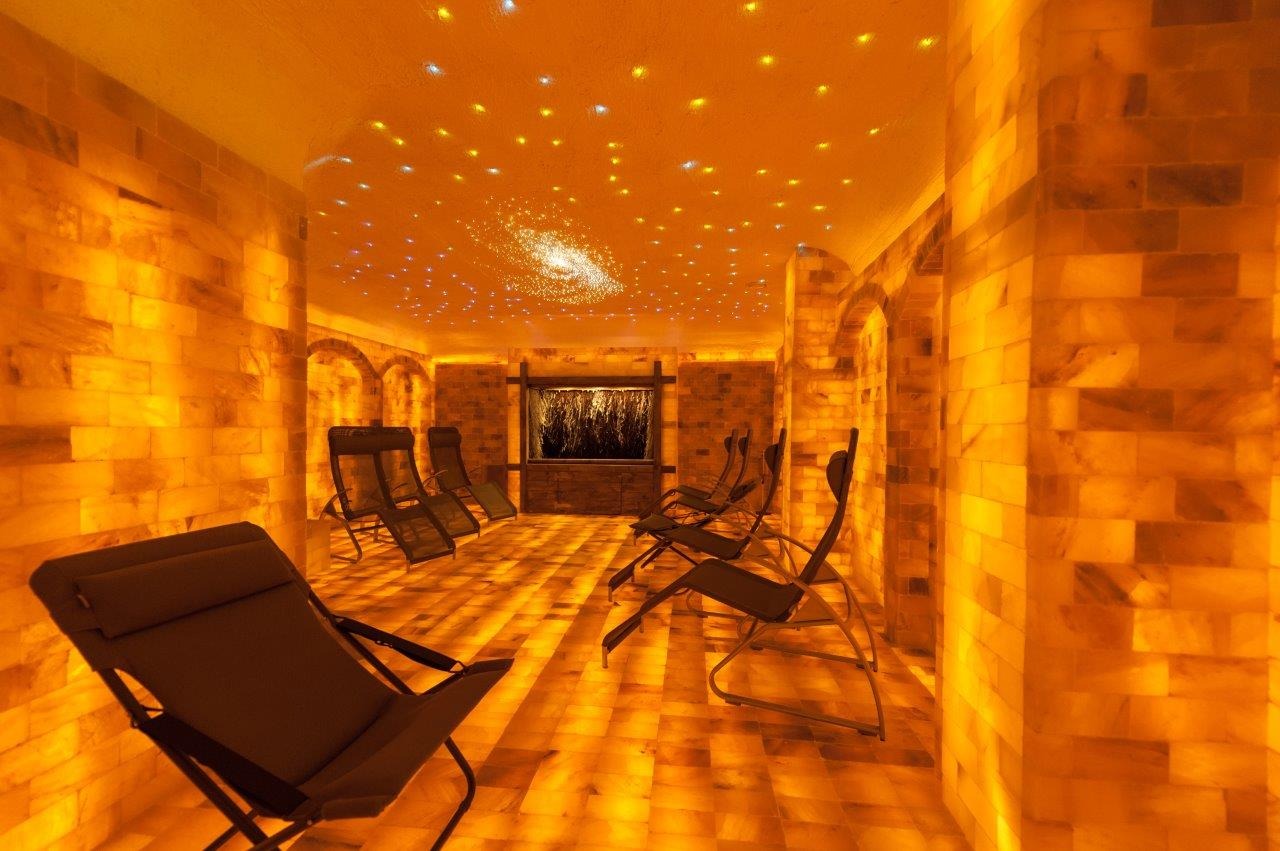 Wnętrze sauny solnej z leżakami, ścianami i podłogą z bloków soli oraz dekoracyjnym oświetleniem sufitowym imitującym gwiazdy.