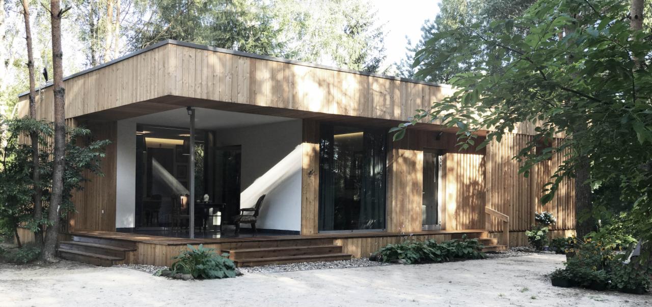 Nowoczesny dom modułowy z drewnianą elewacją, dużymi przeszkleniami i tarasem, otoczony zielenią.