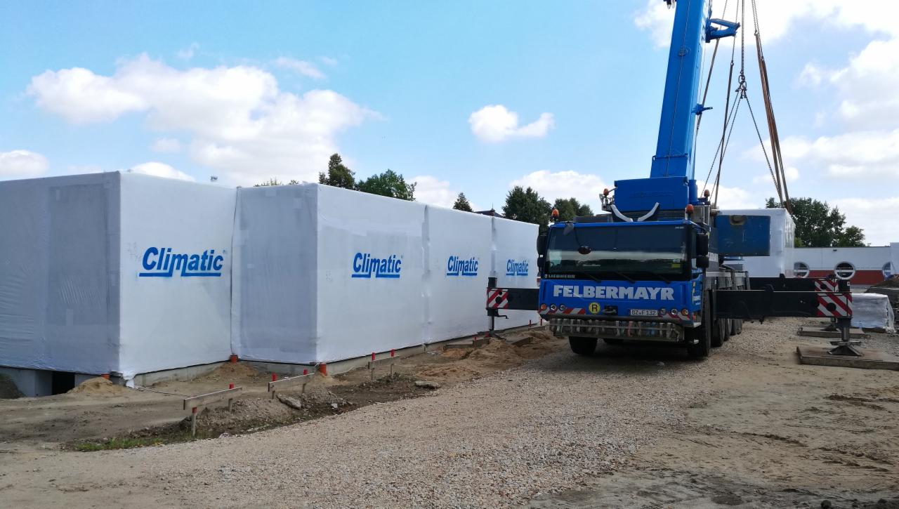 Montaż modułowych segmentów z logo 'Climatic' za pomocą niebieskiego dźwigu firmy Felbermayr na placu budowy.