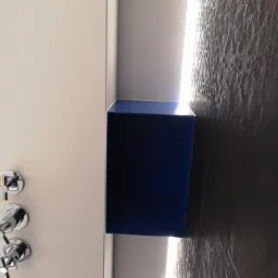 Niebieska metalowa półka wbudowana w ścianę z oświetleniem LED, widoczne zawory prysznicowe.