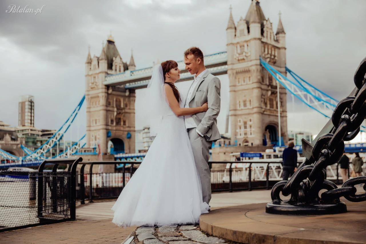 Para młoda w objęciach na tle Tower Bridge w Londynie, z łańcuchem kotwicznym na pierwszym planie.