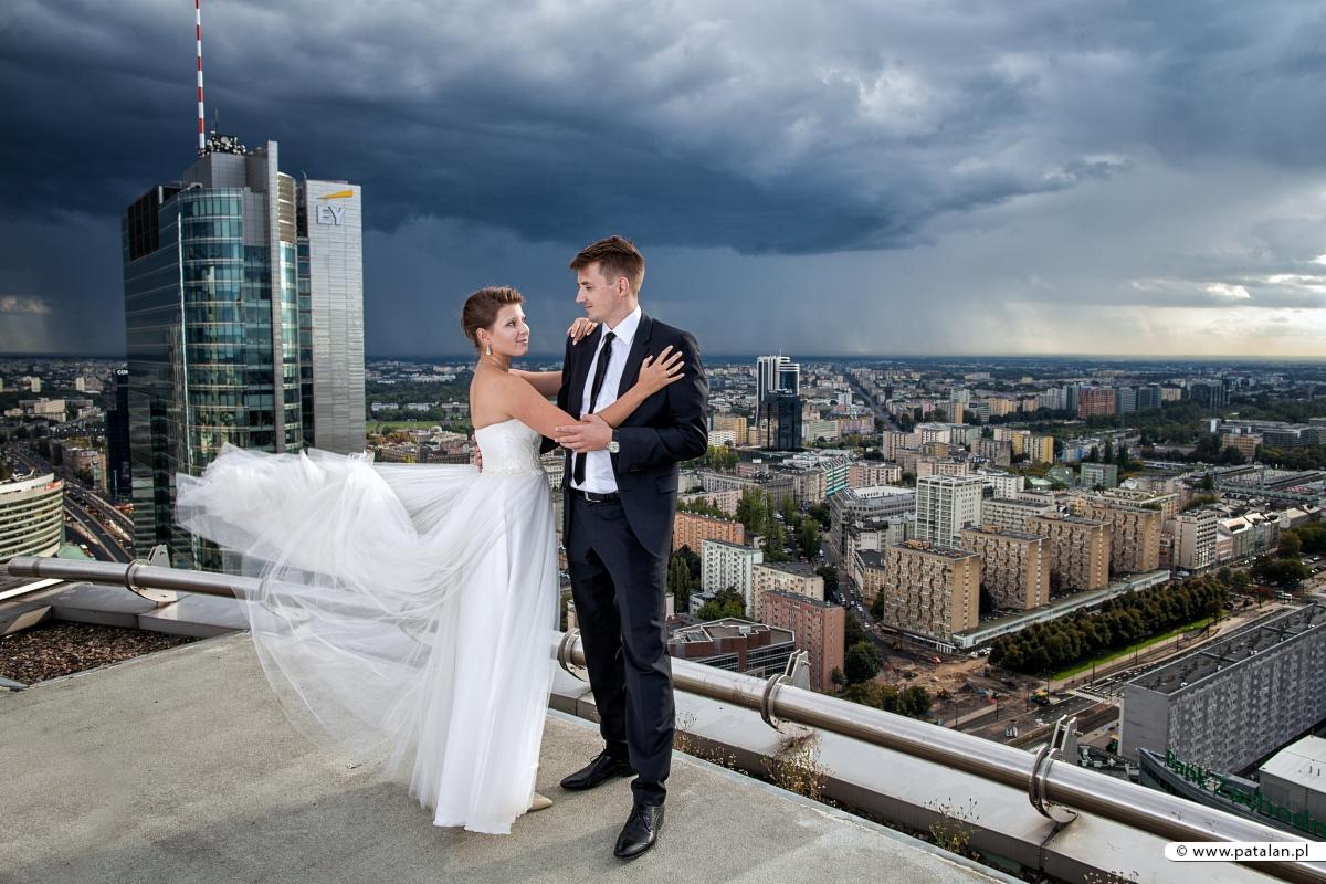 Para młoda w objęciach na dachu wieżowca w Warszawie, w tle burzowe chmury i panorama miasta.