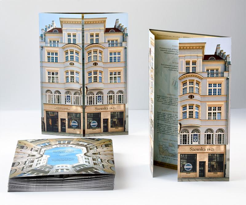 Trójwymiarowa broszura reklamowa przedstawiająca fasadę budynku przy ulicy Szewskiej 19-21, obok stos ulotek z widokiem na dziedziniec budynku, na białym tle.