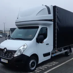 Biały Renault Master z plandeką, zaparkowany na parkingu, widoczny z boku, z numerem rejestracyjnym ST-9839P.
