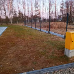 Nowoczesne ogrodzenie panelowe z podmurówką betonową na działce z drzewami. Widoczna skrzynka gazowa przy ogrodzeniu. Realizacja montażu ogrodzenia.