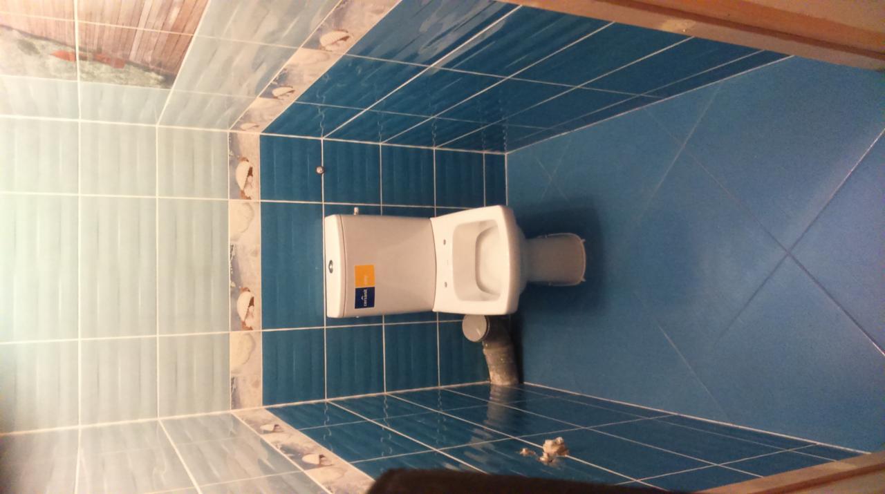 Nowa toaleta wisząca zamontowana w łazience wykończonej niebieską glazurą, widoczne przyłącze kanalizacyjne i fragmenty fugi na podłodze.