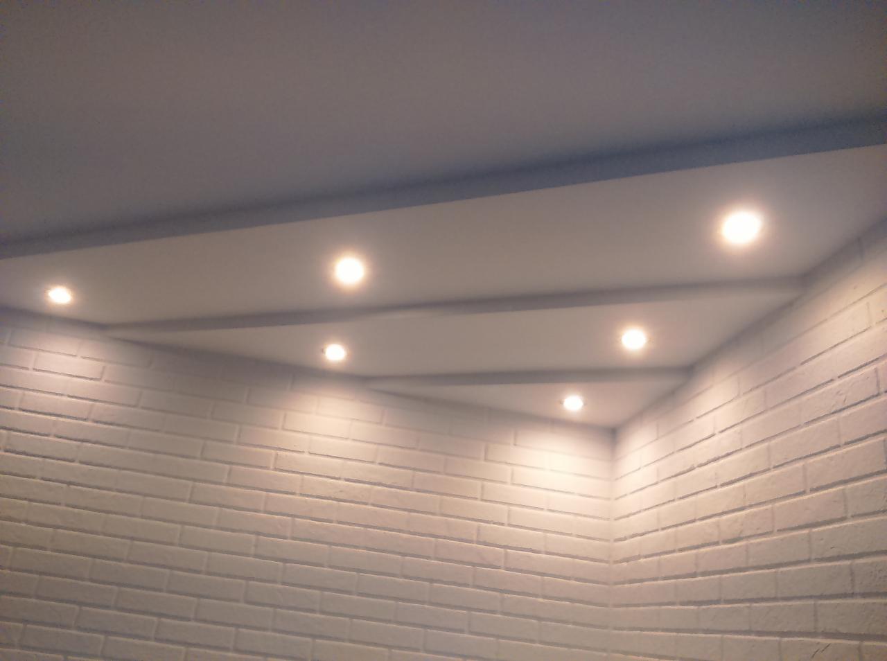 Sufit podwieszany z oświetleniem punktowym LED w pomieszczeniu z białą ścianą z cegły, widok z dołu.