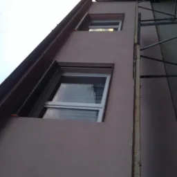 Świeżo otynkowana elewacja budynku z widocznymi oknami i fragmentem rusztowania z boku.