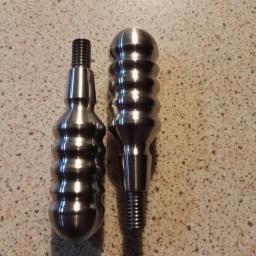 Dar-Tec CNC - Dwa metalowe uchwyty z gwintem, jeden z kulistą główką i żłobieniami, drugi bardziej smukły, leżące na nakrapianym blacie.