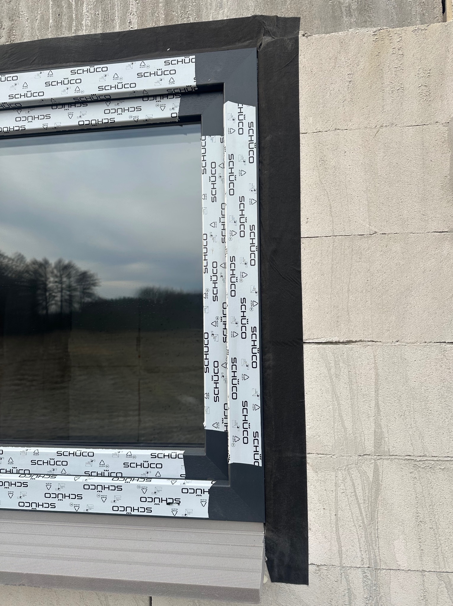 Montaż okna w surowym murze, widoczne folie uszczelniające i taśmy ochronne producenta na ramie.