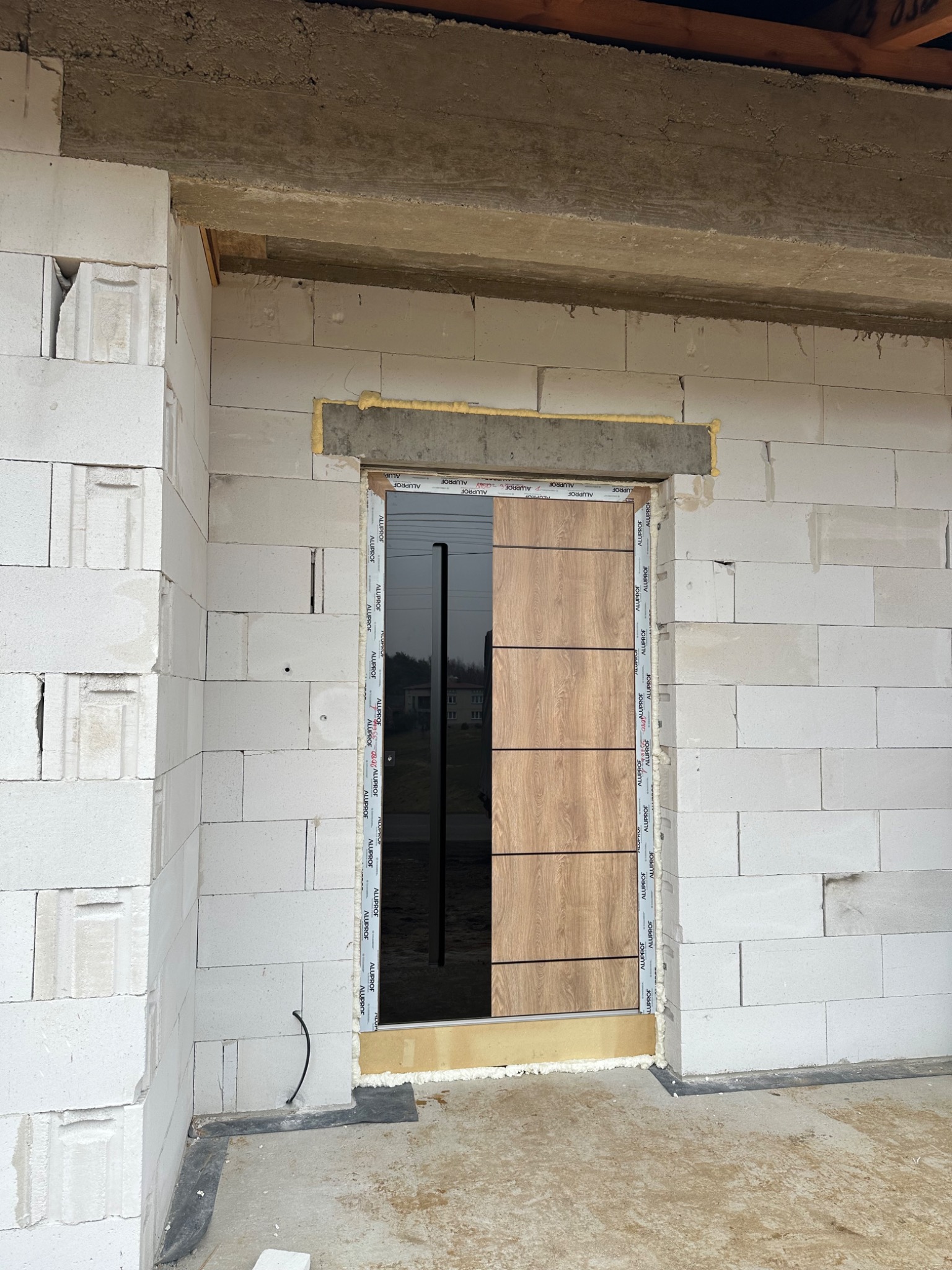 Montaż okna w surowym stanie. Widoczne bloczki z betonu komórkowego, pianka montażowa uszczelniająca ramę okienną oraz częściowo zamontowana listwa przypodłogowa.