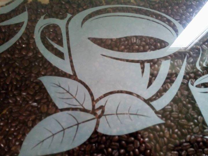 Piaskowany wzór filiżanki kawy i liści na szklanej powierzchni z tłem z ziaren kawy.