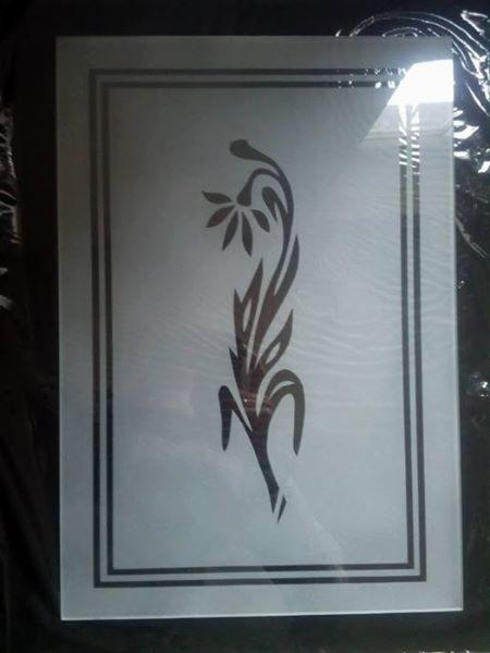Szklana tafla z dekoracyjnym, matowym wzorem roślinnym i podwójną ramką, na ciemnym tle.