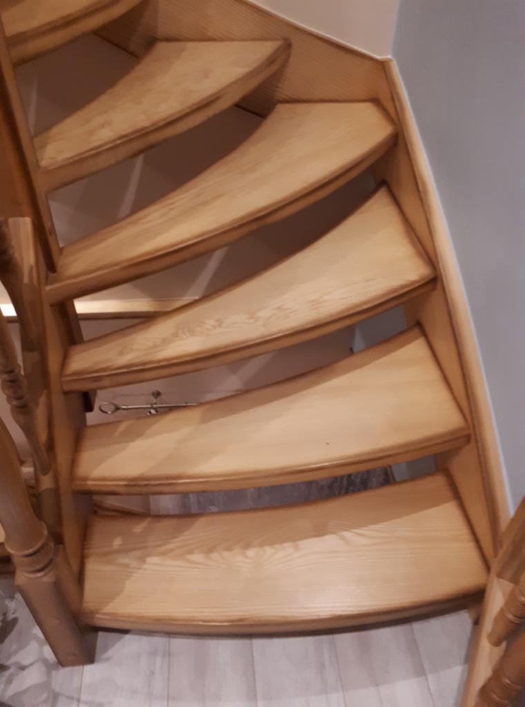 Klatka schodowa z jasnego drewna z kręconymi schodami, widok z dołu, z widocznym mocowaniem w ścianie.