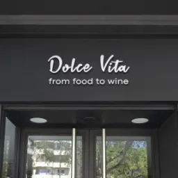 Elegancki szyld nad wejściem do restauracji 'Dolce Vita' z napisem 'from food to wine', wykonany w białej czcionce na ciemnoszarym tle.