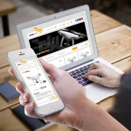 Prezentacja sklepu internetowego z dronami na laptopie i smartfonie, widok z perspektywy osoby wpisującej tekst na klawiaturze laptopa, na ekranach identyczny układ strony z ofertą dronów.