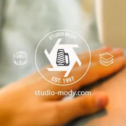 Logo firmy Studio Mody z Pabianic, przedstawiające szpule nici w okręgu i rok założenia 1997, na rozmytym tle maszyny do szycia i dłoni pracownika.