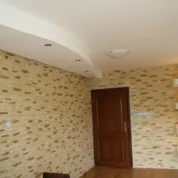 Wykończone wnętrze z dekoracyjną ścianą imitującą kamień, podwieszanym sufitem z oświetleniem punktowym i drewnianymi drzwiami.