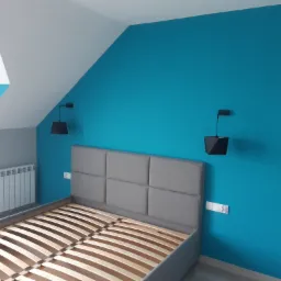 Sypialnia na poddaszu z turkusową ścianą, szarym zagłówkiem łóżka i minimalistycznymi lampkami nocnymi.