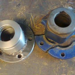 PPUH WOMAR - Porównanie dwóch metalowych elementów kołnierzowych: nowy, pospawany element obok pękniętego, zniszczonego elementu pomalowanego na niebiesko, leżących na brudnym metalowym stole.