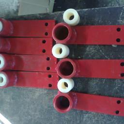 PPUH WOMAR - Czerwone, metalowe elementy z przyspawanymi uchwytami i włożonymi białymi tulejami z tworzywa sztucznego, ułożone rzędami na brudnym stole warsztatowym.