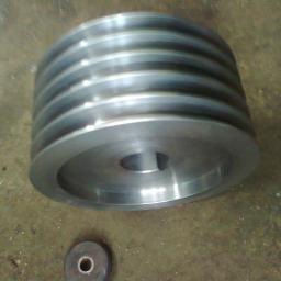 PPUH WOMAR - Metalowa, wielorowkowa rolka pasowa z otworem na klin, obok mały, okrągły element, leżąca na brudnej, metalowej powierzchni.