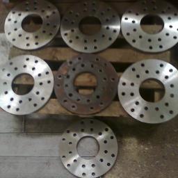 PPUH WOMAR - Siedem metalowych tarcz z otworami ułożonych na drewnianej palecie, jedna tarcza pokryta rdzą.