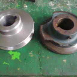 PPUH WOMAR - Porównanie nowej, błyszczącej, metalowej rolki pasowej z uszkodzoną, skorodowaną rolką na zielonym, pomalowanym stole warsztatowym.