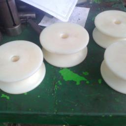 PPUH WOMAR - Cztery białe, plastikowe rolki z otworem w środku, ułożone na zielonym, pomalowanym stole warsztatowym z widocznymi śladami użytkowania i narzędziami w tle.