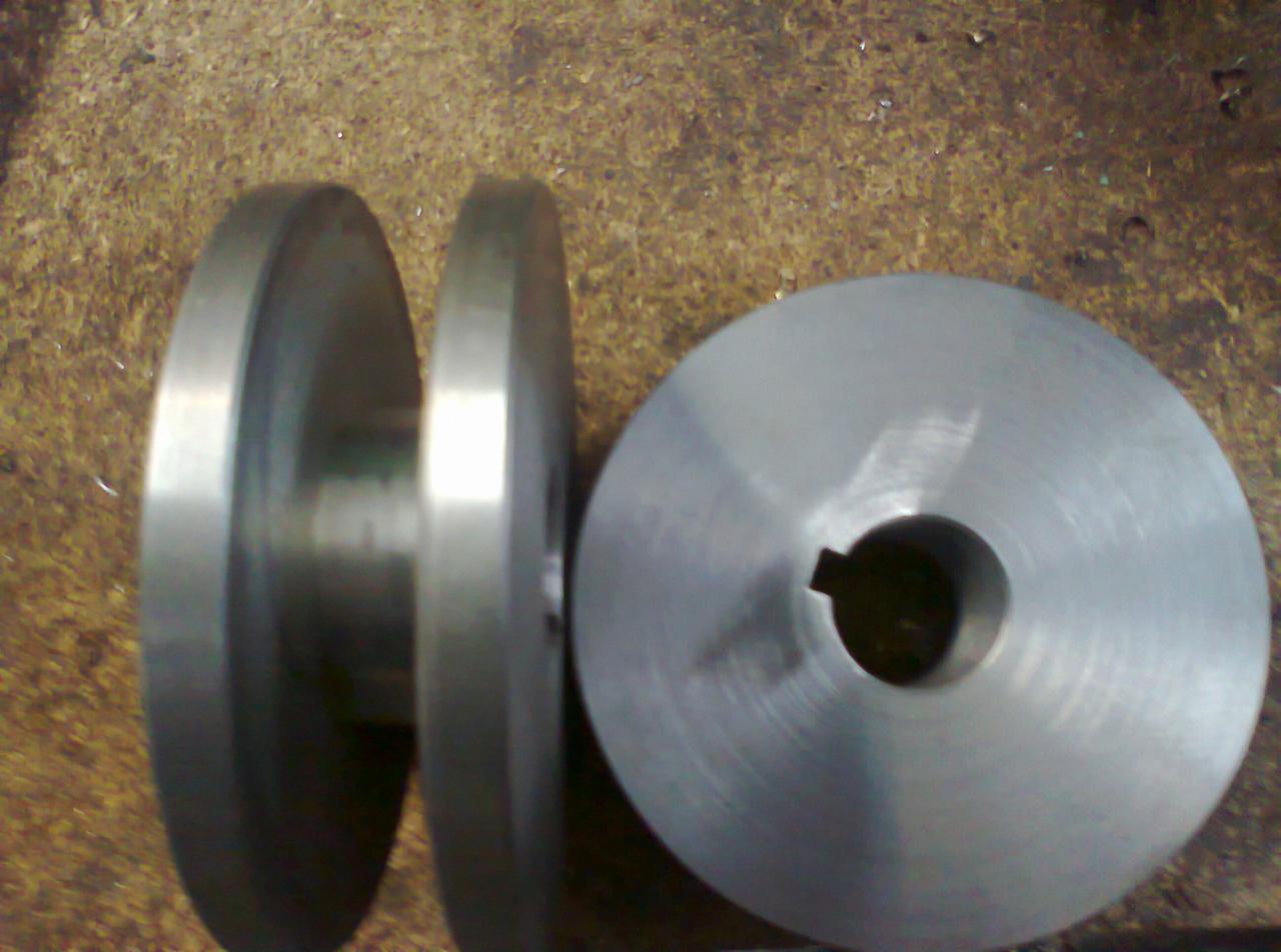 Dwa metalowe koła pasowe o różnych rozmiarach, jedno z otworem na wpust, leżące na brudnej powierzchni warsztatowej.