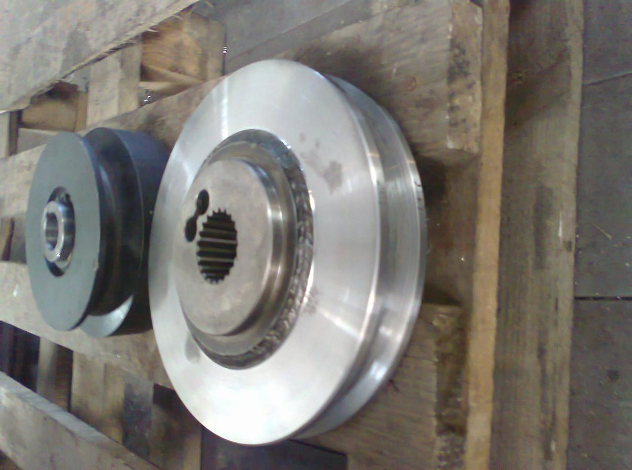 Dwa metalowe koła pasowe o różnych rozmiarach, jedno z widocznym wielowypustem, leżące na drewnianej palecie.