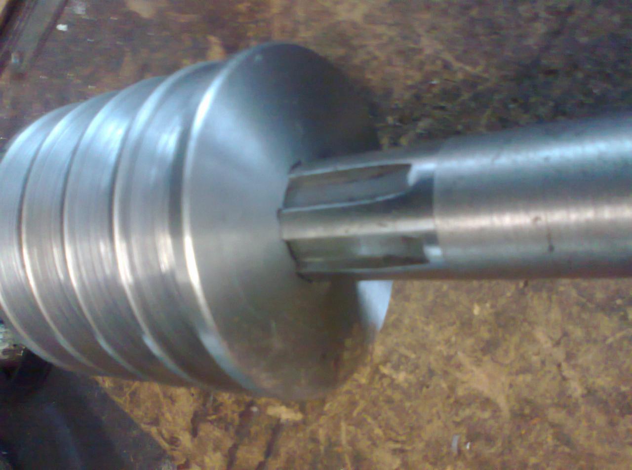 Metalowy wał z wielowypustem i gwintem trapezowym, obrobiony na tokarce, widoczne ślady obróbki.