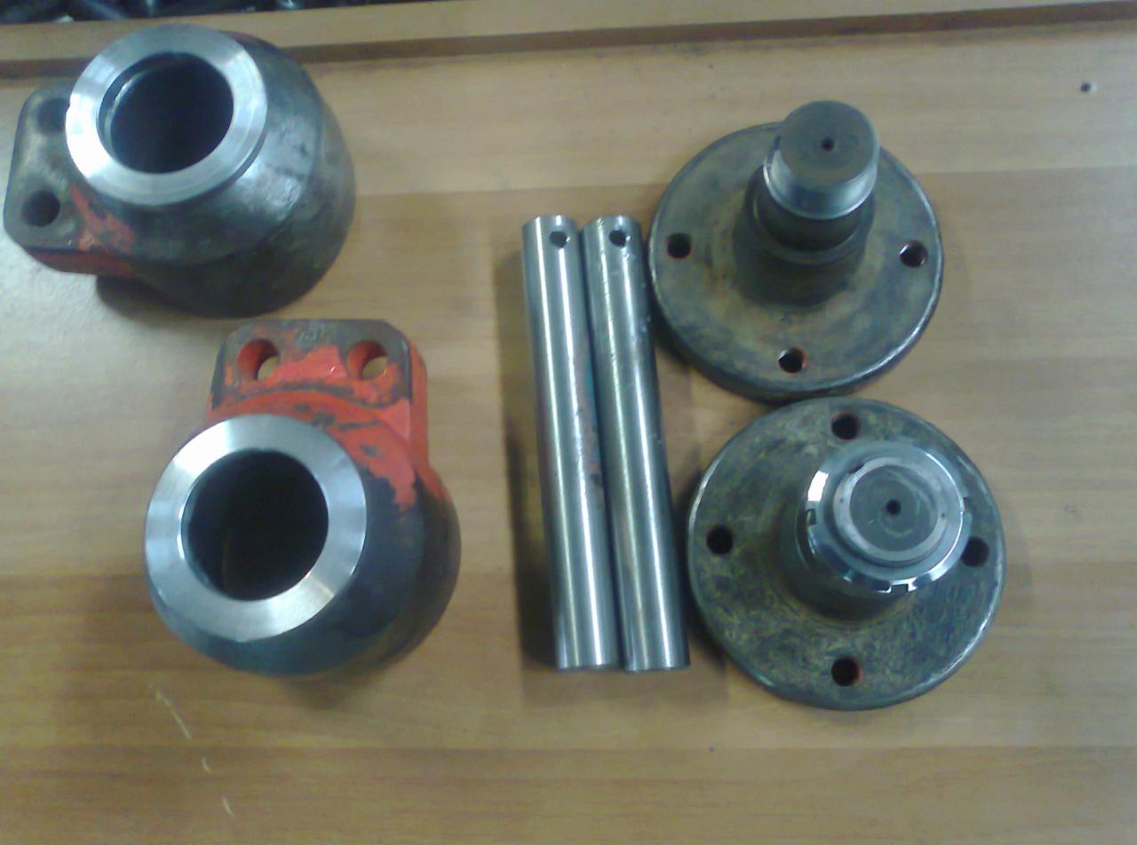 Detale metalowe: dwa elementy z czerwonymi fragmentami farby, dwa metalowe walce i dwa kołnierze z piastami, leżące na drewnianym blacie.