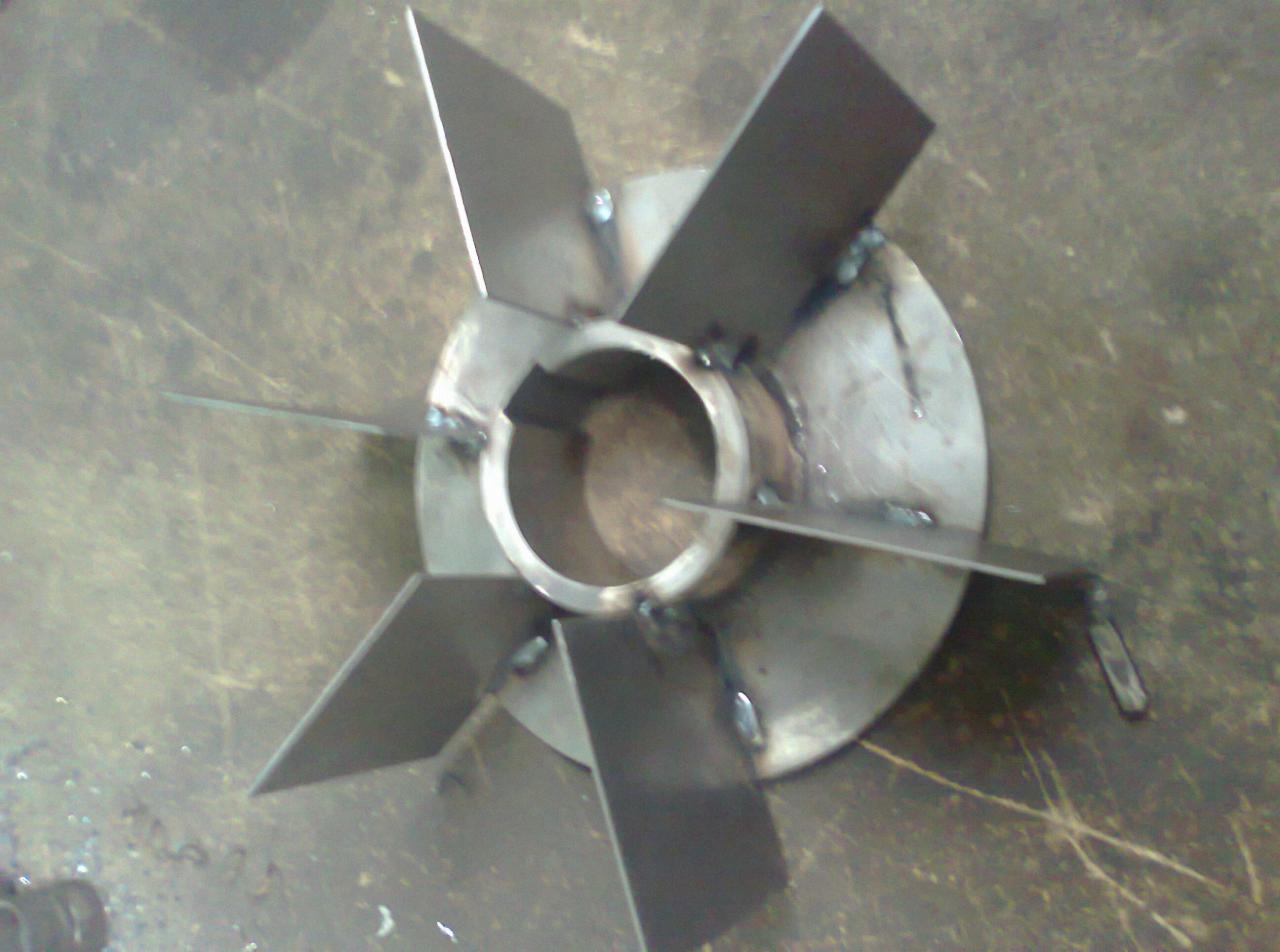 Metalowa turbina z przyspawanymi łopatkami, widoczne spawy na obwodzie tarczy i wokół piasty, surowy metal na tle szarej, zabrudzonej powierzchni.