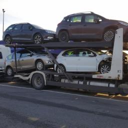 BUBU Robert Bruzi - Laweta przewozi uszkodzony biały samochód osobowy oraz trzy inne pojazdy, w tym przyczepę kempingową Hobby, na dwupoziomowej platformie transportowej.
