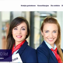 Dwie uśmiechnięte kobiety w granatowych marynarkach i czerwonych apaszkach, reprezentujące firmę finansową Fines Operator Bankowy, na tle biura.