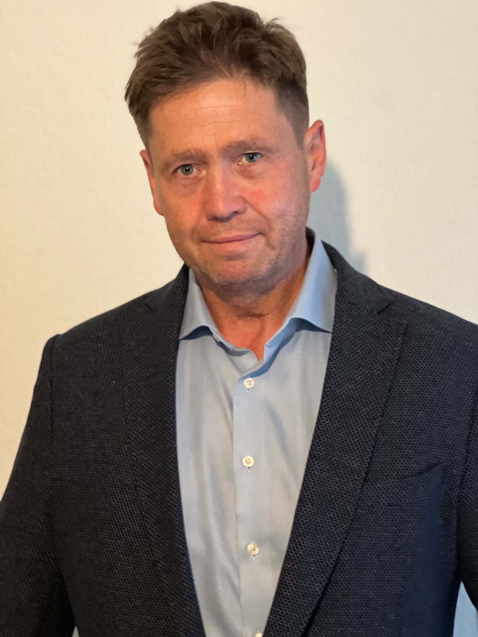 Portret mężczyzny w błękitnej koszuli i ciemnej marynarce na jasnym tle.