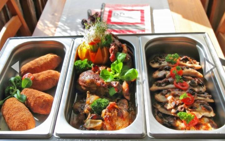 Bufet z potrawami: krokiety, duszone mięso z warzywami i grzanki z pieczarkami, ułożone w metalowych pojemnikach.