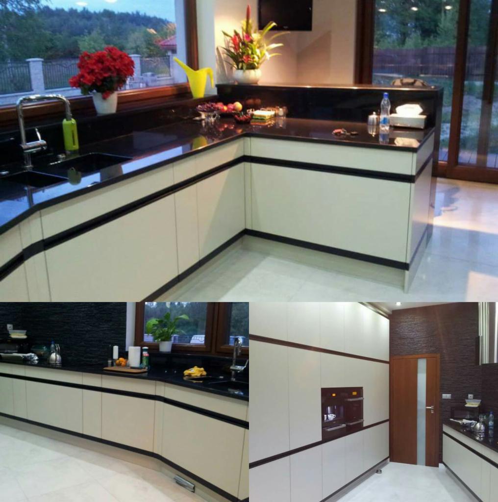 Nowoczesna kuchnia z białymi szafkami, czarnym blatem i elementami dekoracyjnymi, w tym kwiatami w oknie i owocami na blacie.