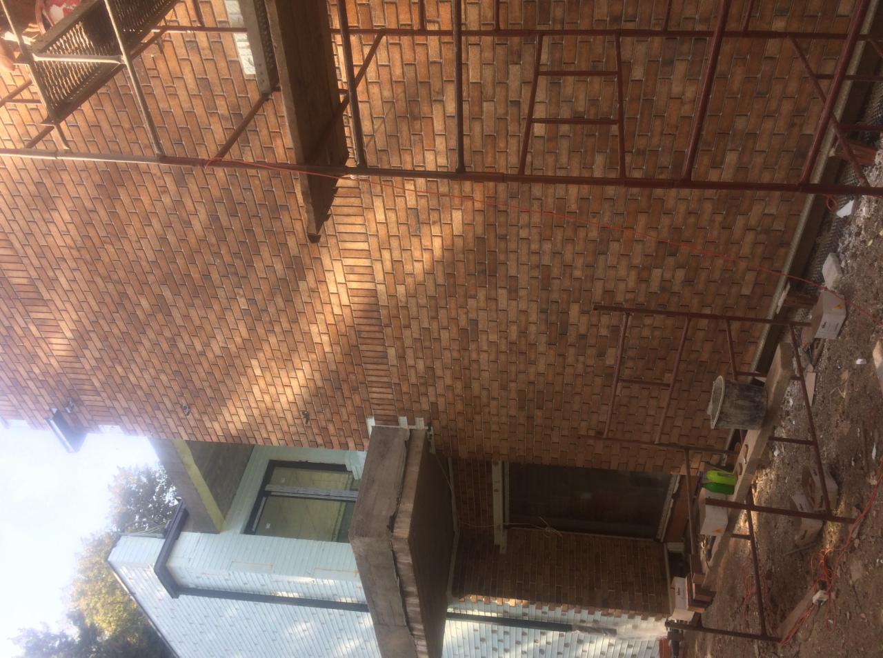 Ściana budynku w trakcie wykańczania z cegły klinkierowej, widoczne rusztowania i fragment ocieplonej ściany z oknem.