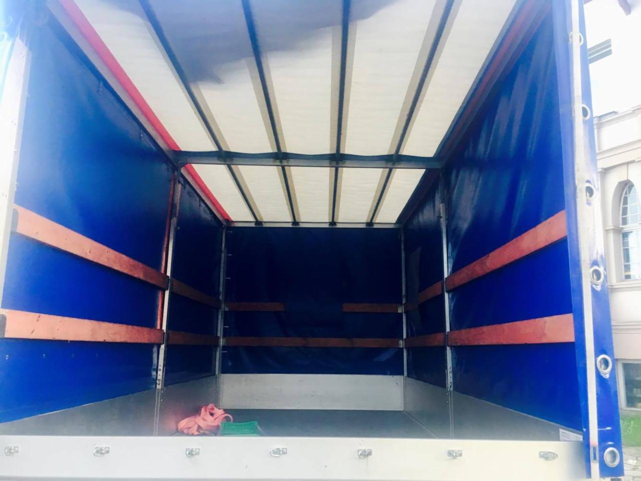 Wnętrze paki samochodu dostawczego z plandeką, widoczne mocowania i podłoga, na podłodze leżą szmaty.