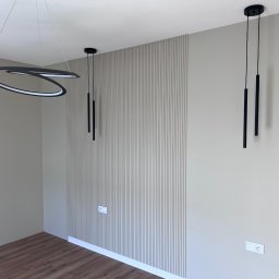 WIERZBIAK Marek Wierzbiak - Nowoczesne wykończenie wnętrza: panel ścienny z pionowymi listwami w odcieniach beżu, designerskie lampy wiszące i drewnopodobna podłoga. Minimalistyczny styl.