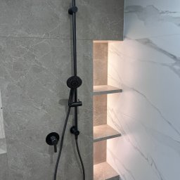 WIERZBIAK Marek Wierzbiak - Nowoczesna kabina prysznicowa z czarną armaturą i podświetlanymi półkami wnękowymi, wykończona płytkami imitującymi marmur.