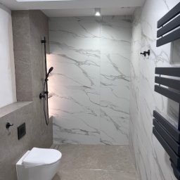 WIERZBIAK Marek Wierzbiak - Nowoczesna łazienka z marmurowymi płytkami, wiszącą toaletą i czarną armaturą. Minimalistyczny design, jasne wnętrze z akcentami szarości i bieli.